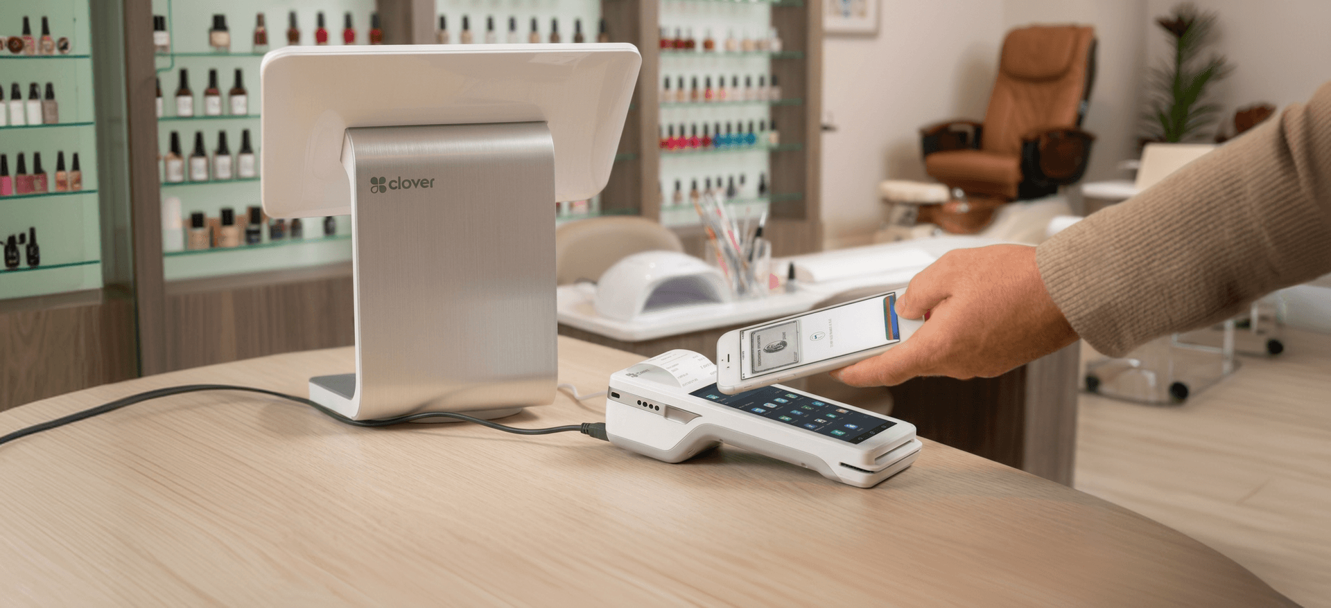 A customer tapping a phone on a Clover terminal at a nail salon counter